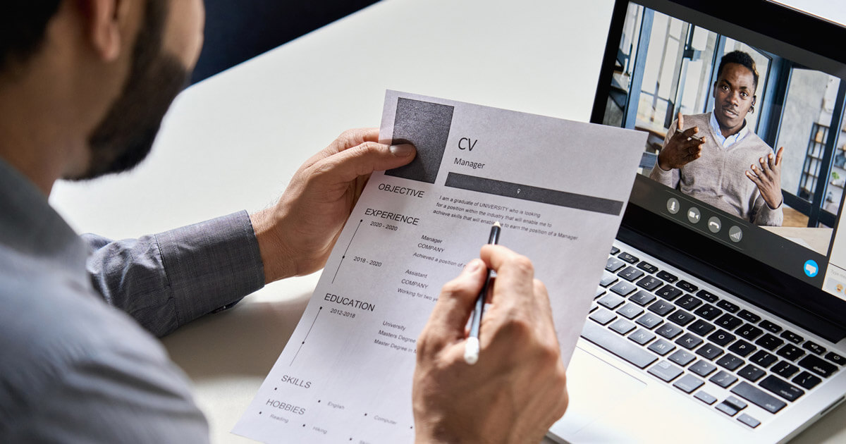 A man holds a CV resume while a laptop rests on the table beside him, indicating a moment of interviewing.